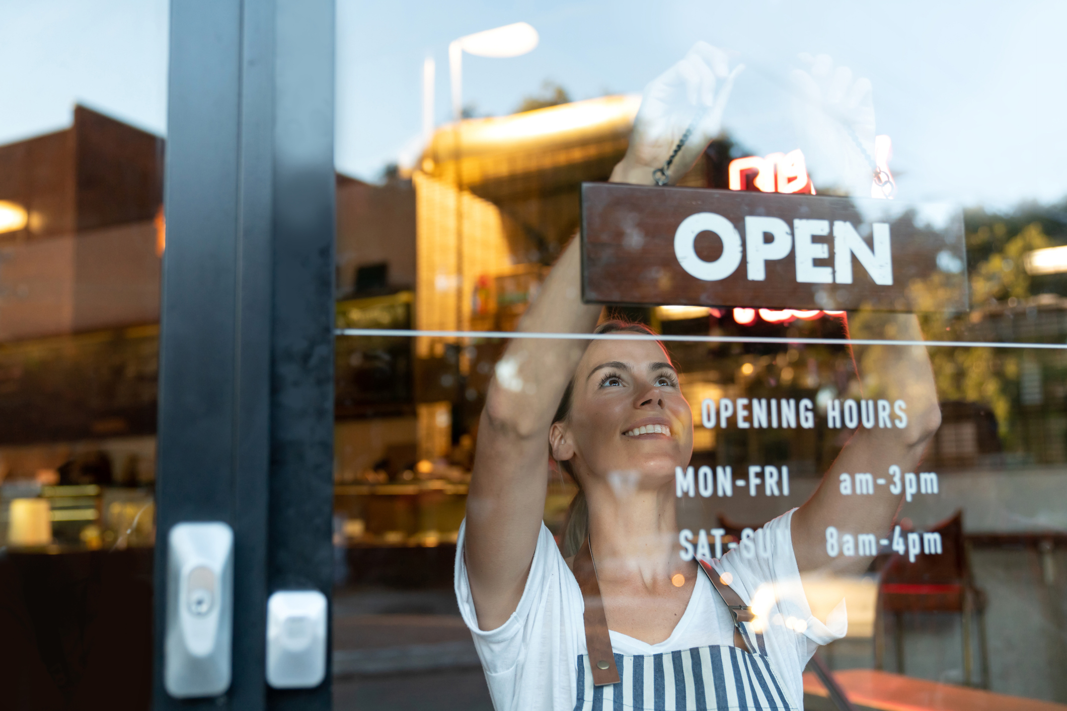 Happy business owner hanging an open sign at a cafe: Latest GDP figures highlight the importance of hospitality in aiding economic recovery