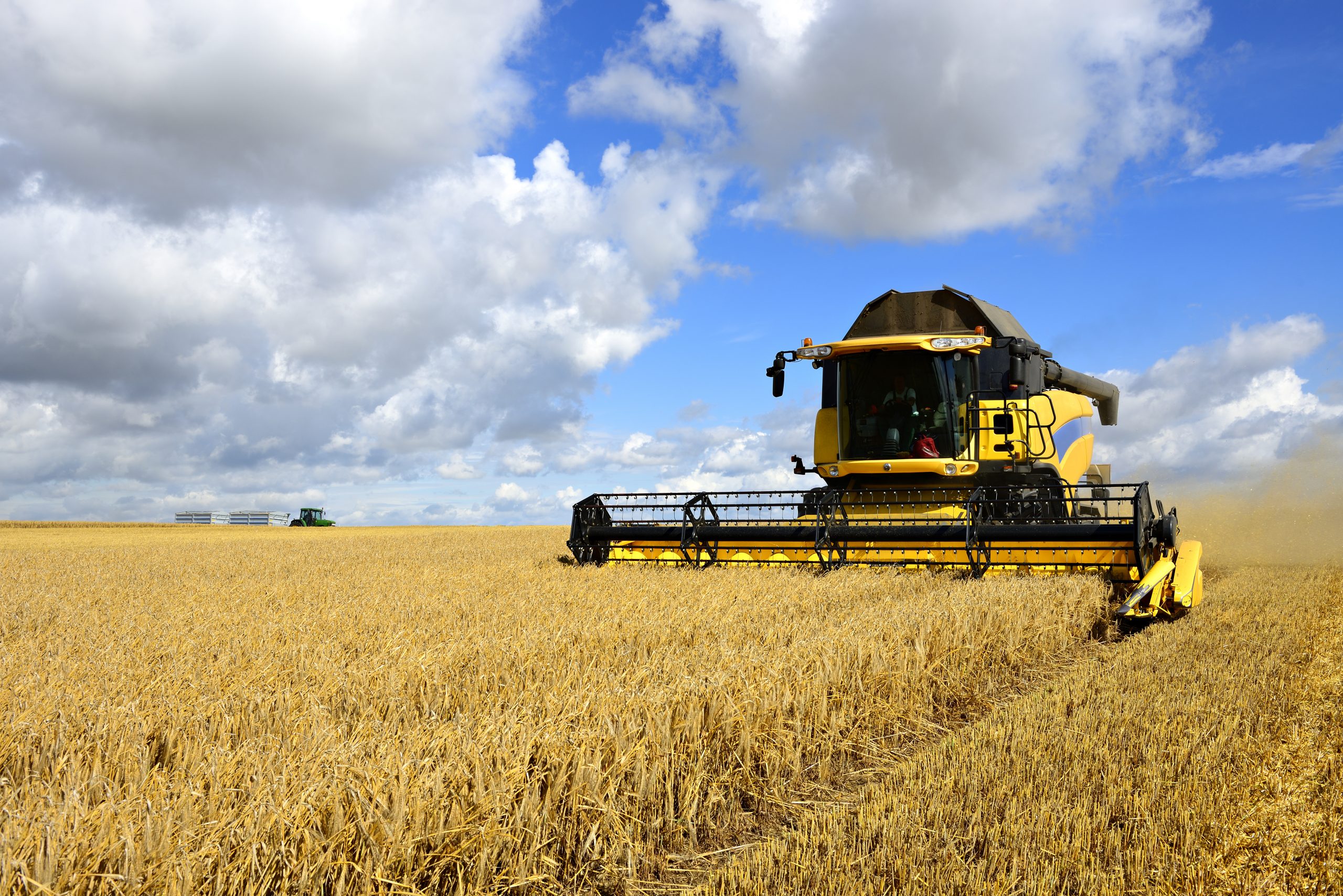 Combine Harvester and Tractor in Barley Field during Harvest: Heineken UK launches low carbon barley trial