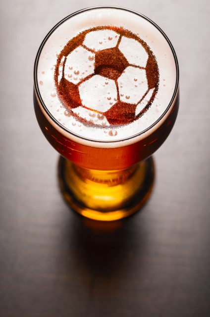 soccer or football ball symbol on foam in beer glass on black table, view from above: England quarter final World Cup match could give £6m boost to UK pubs