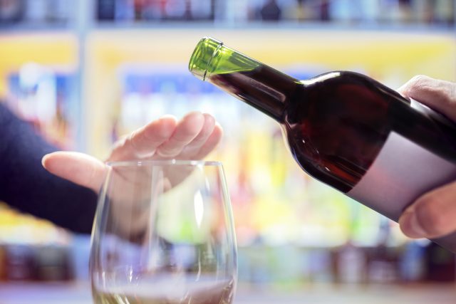 Mano femminile che rifiuta altro alcol dalla bottiglia di vino in un bar: In Francia la generazione più anziana è accusata del calo del vino domestico