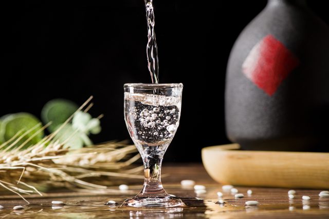 chinese liquor spirits drink is poured into a glass from a bottle on wood background: China's top brewer buys into baijiu market