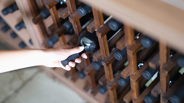 Woman chooses bottle of wine in cellar closeup. Expensive collectible red wines concept: Berry Bros & Rudd encourages investors to look beyond Burgundy and Bordeaux