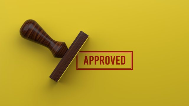 A wooden rubber Stamp marks a surface with "Approved," symbolizing Success, Acceptance, and Validation. This positive Concept is perfect for illustrating a successful outcome in Business, passing a Test, or receiving official authorization. The image represents a final, positive Decision and a high level of Achievement and Quality Control.