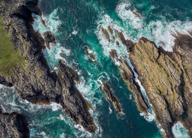 aerial photo of rock cliffs with wild ocean surf at Strathy point in northern Scotland, UK